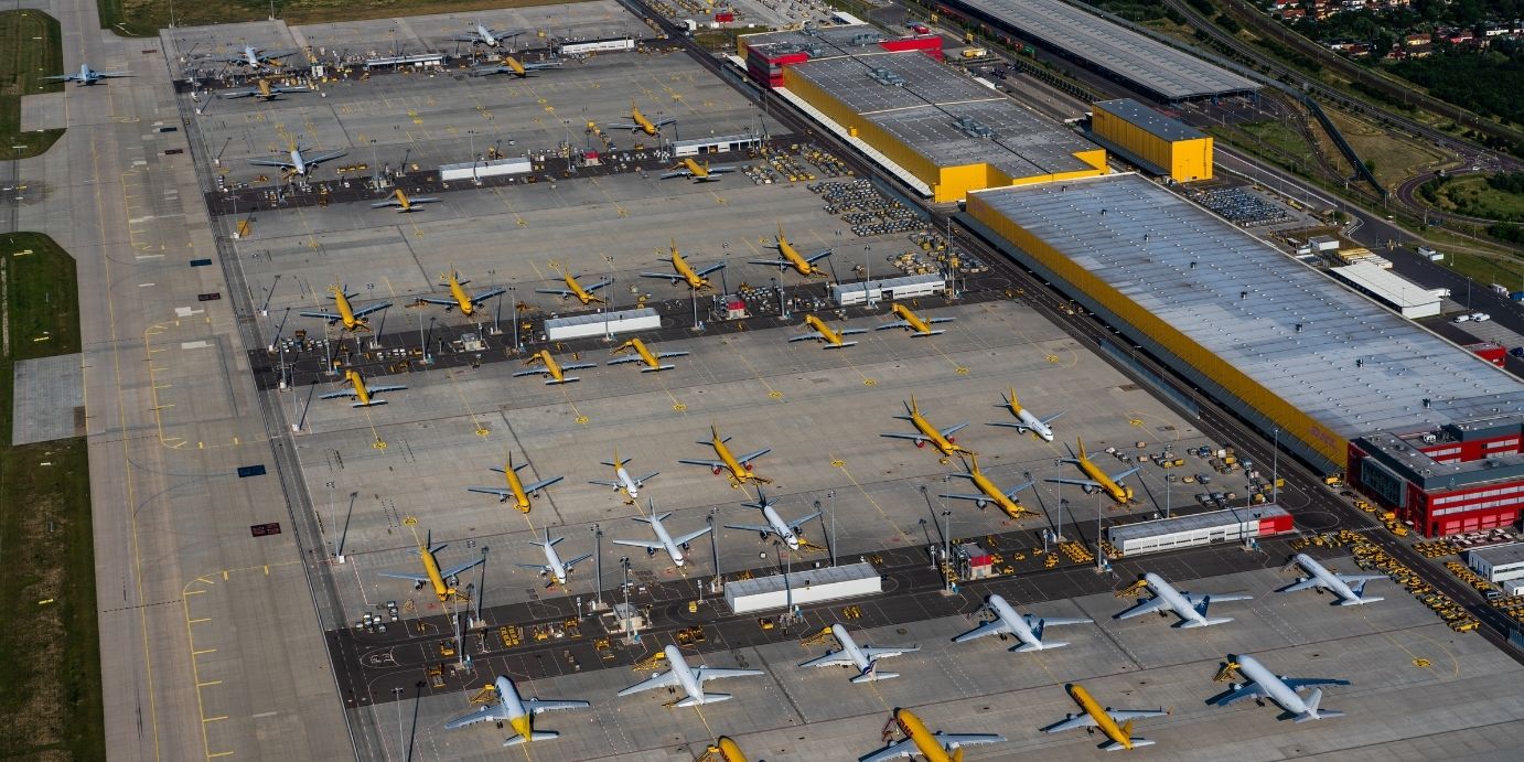 Luftaufnahmen des DHL-Frachtzentrums am Flughafen Leipzig/Halle, die das Hauptfrachtvorfeld, Gebäude, Hangars und mehrere geparkte Flugzeuge zeigen.