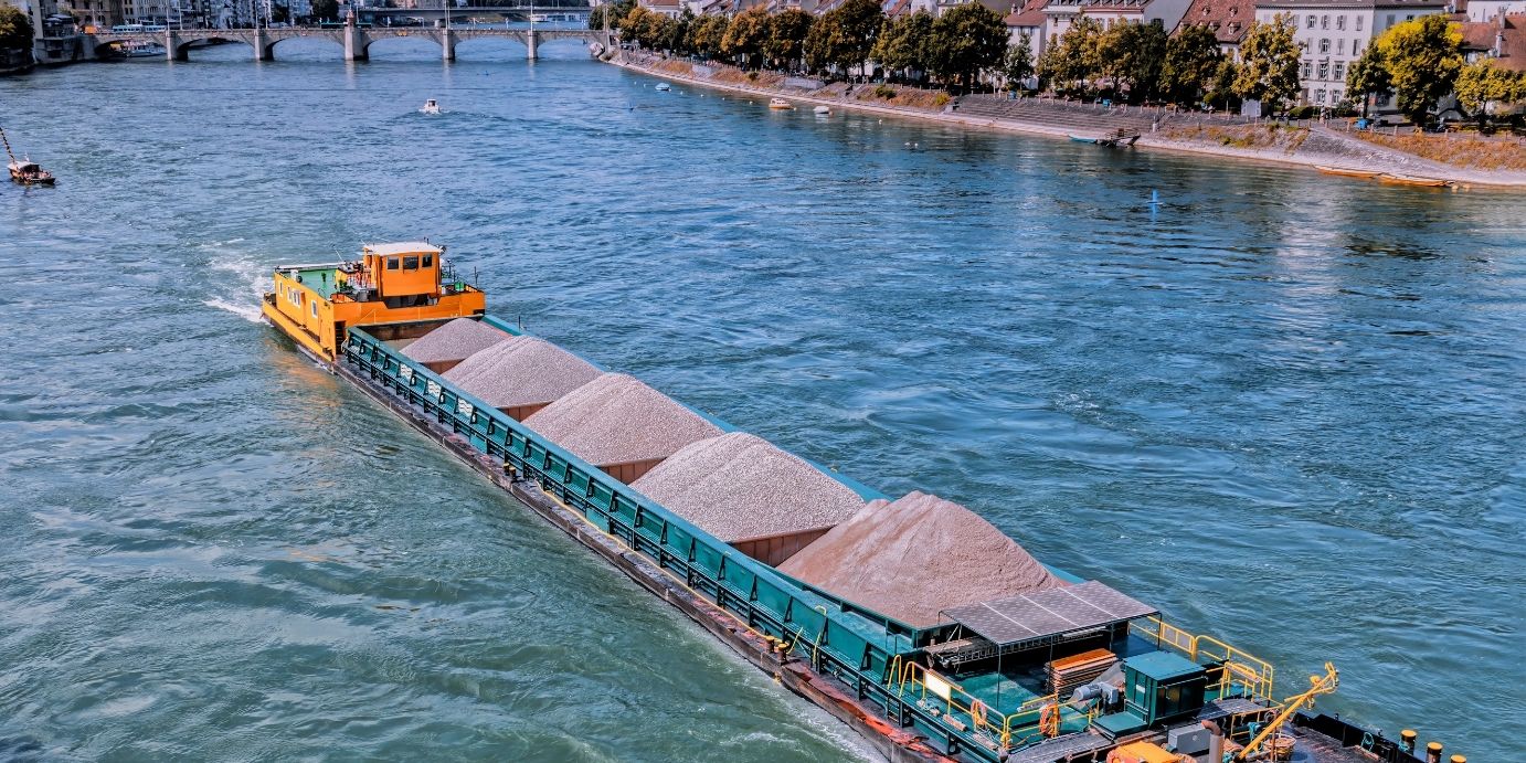 Ein großes Containerschiff beim Transport bunter Frachtcontainer auf dem Rhein nahe dem Hafen Weil am Rhein, im Hintergrund die Dreiländerbrücke.